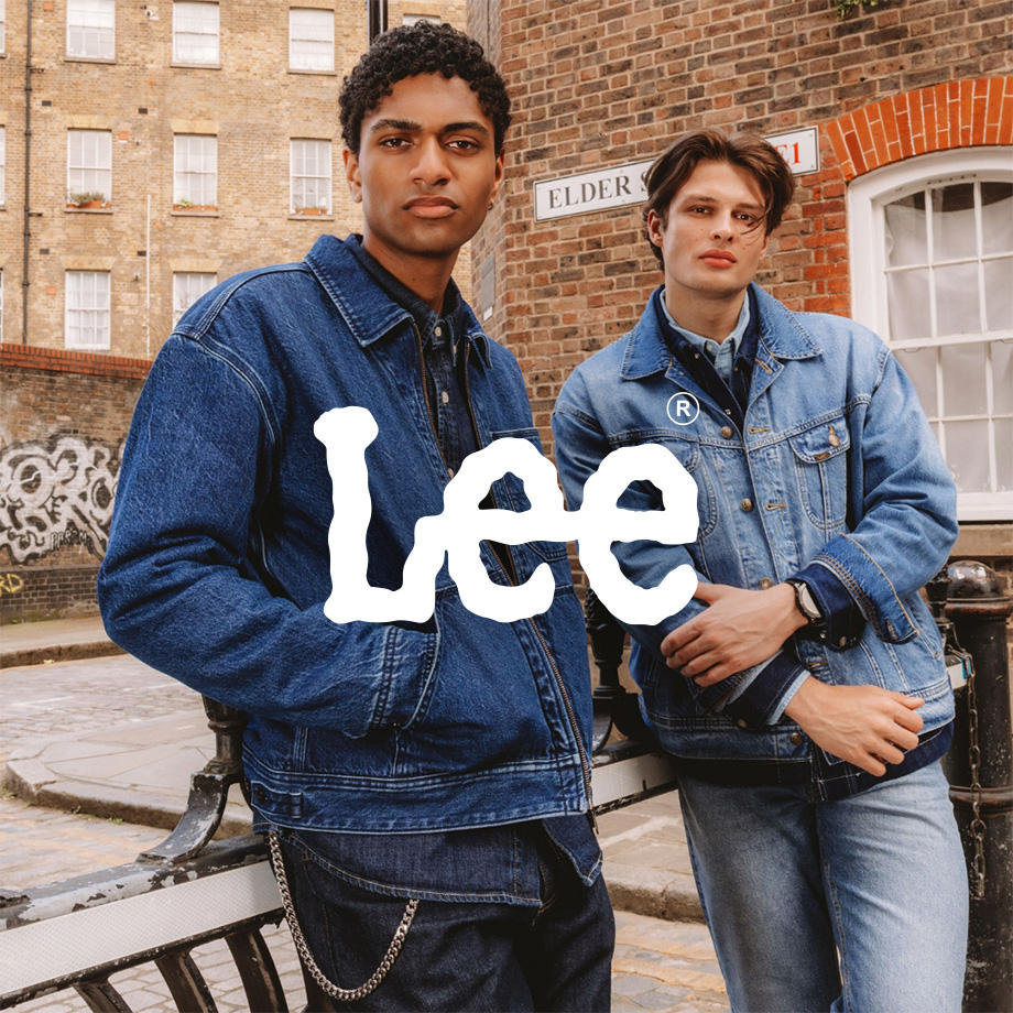 Ein Markenbild von der Marke "Lee". Zwei junge Männer posieren selbstbewusst auf einer Straße vor Backsteinfassaden. Beide tragen Denim-on-Denim-Looks mit Jeansjacken und -hosen von Lee – einer in dunklem, der andere in hellem Denim. Der urbane Look wirkt zeitlos und cool im Londoner Street-Style-Flair.