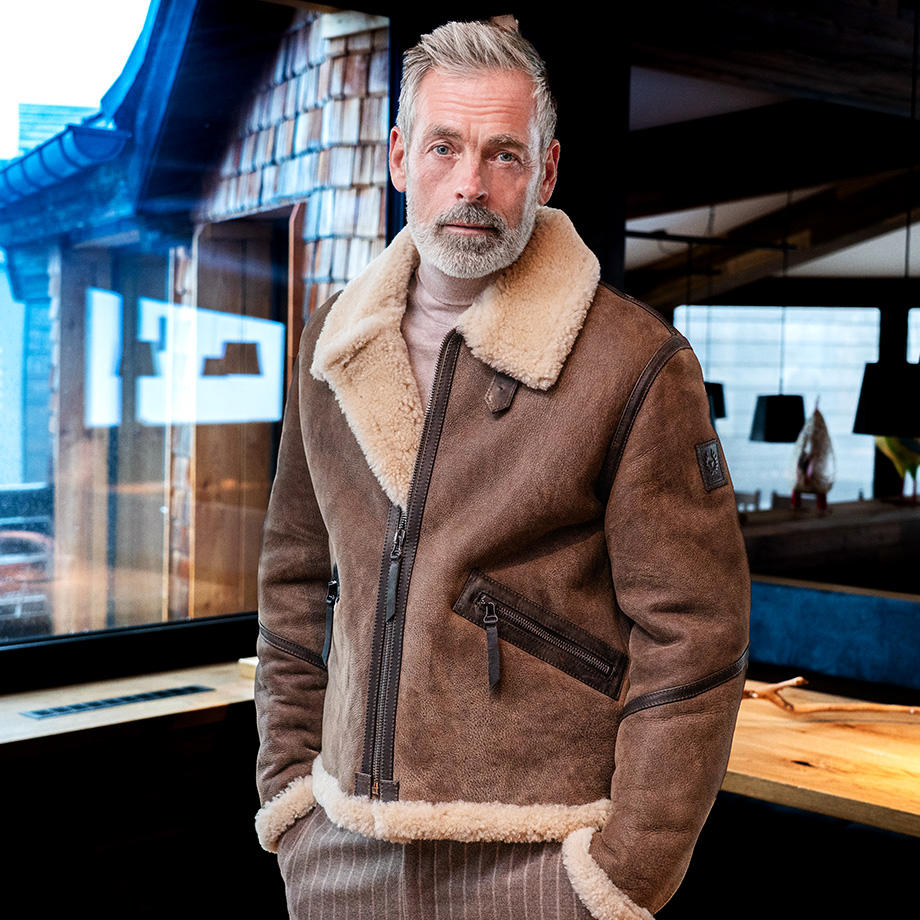 Mann trägt braune Leder-Fliegerjacke mit Lammfellbesatz von Belstaff in urbanem Setting