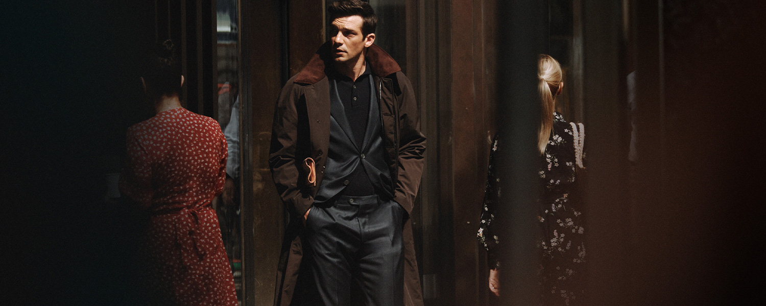 Eleganter Mann trägt Oscar Jacobson Anzug mit braunem Mantel stilvoll in urbaner Umgebung.