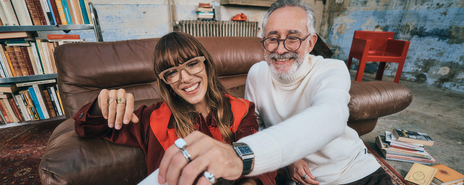 Frau und Mann tragen moderne Brillen von Izipizi, sitzen lächelnd auf einem Ledersofa in gemütlicher Loft-Atmosphäre – stylische Lesebrillen und Eyewear für jedes Alter.