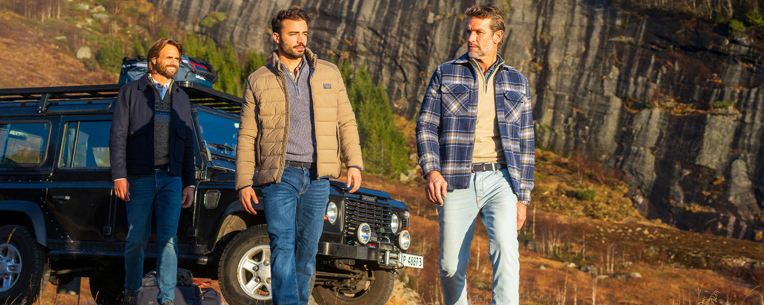Drei Männer in N.Z.A. Outdoor-Mode mit Jacken und Jeans vor einem Geländewagen in bergiger Landschaft.