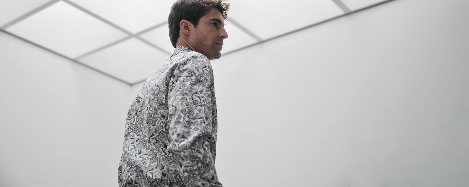 Mann trägt ein elegantes Eterna Hemd mit schwarz-weißem Muster, modern inszeniert in minimalistischer Architektur.
