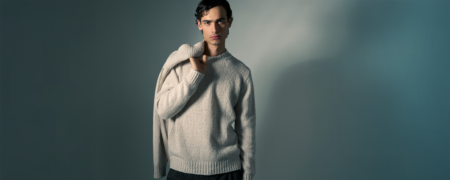 Mann trägt cremefarbenen Strickpullover von Daniele Fiesoli und hält lässig einen zweiten Pullover über die Schulter – elegante italienische Knitwear für Herren.
