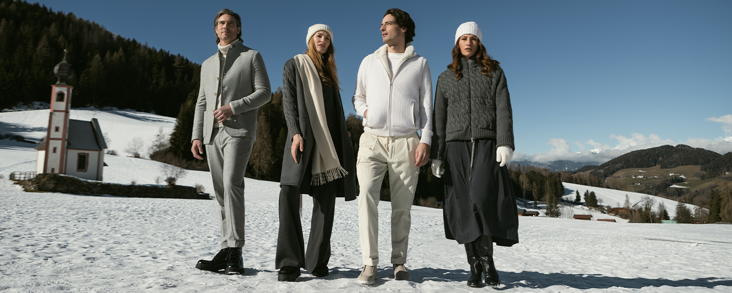 Gran Sasso Wintermode – elegante Strickjacken, Pullover und Mäntel für Damen und Herren in Grau und Weiß, stilvoll kombiniert im verschneiten Alpen-Panorama.