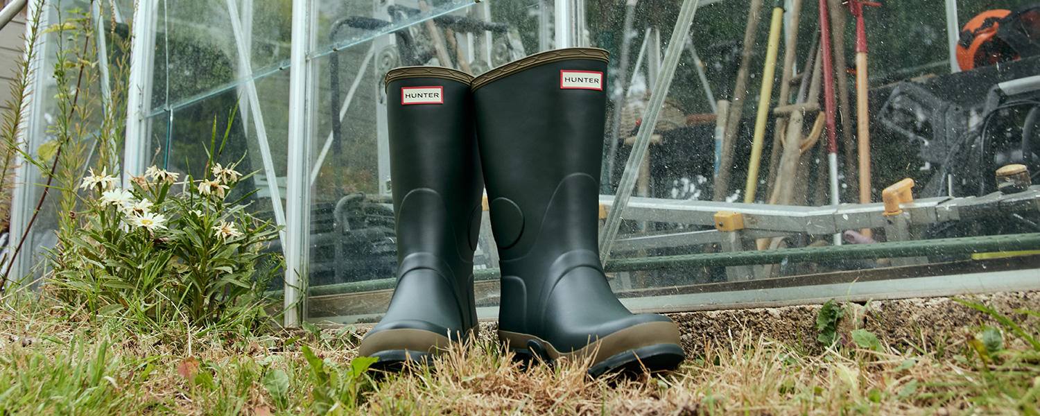 Grüne Hunter Gummistiefel stehen vor einem Gewächshaus im Garten.