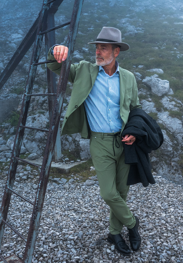 Junger Mann in einem eleganten hellgrauen dreiteiligen Anzug und Nickituch steht in einem, grünen Gartenambiente.