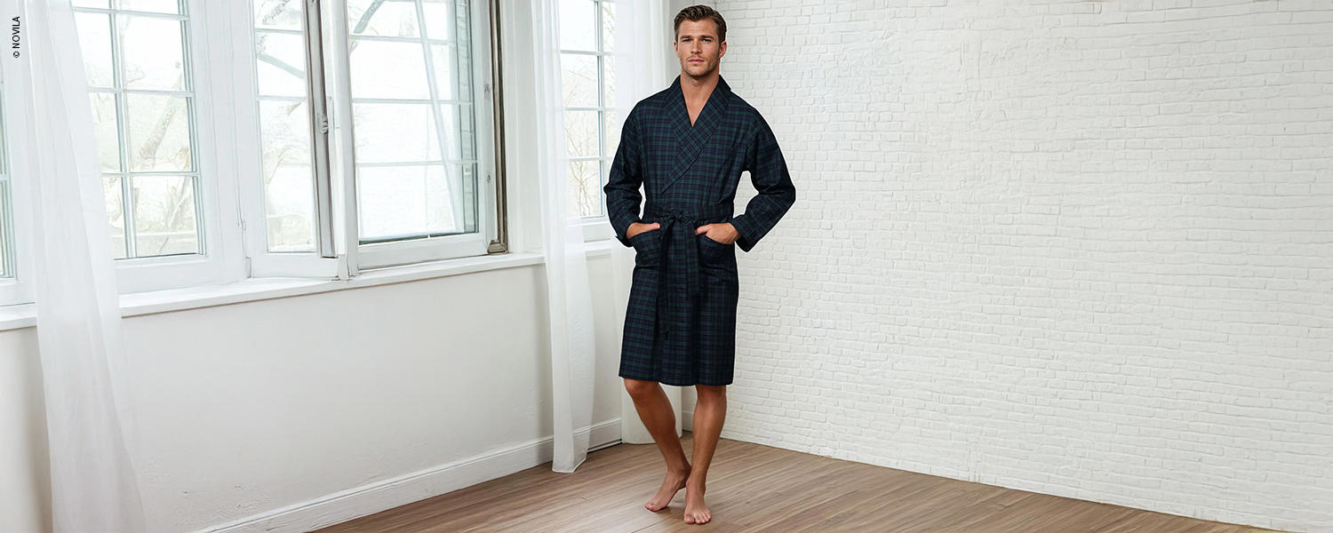 Ein Mann trägt einen karierten Hausmantel mit Gürtelbindung und Taschen, perfekt für entspannte Stunden zuhause.