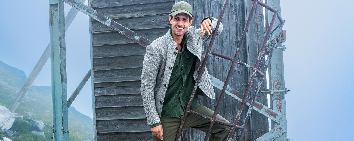 Auf dem Bild trägt ein Mann ein graues Casual-Sakko über einem grünen Hemd, kombiniert mit einer Cap – ein entspannter, stilvoller Look.