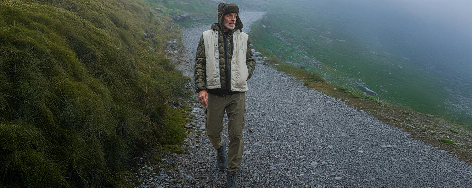Olivgrüne Cargohose mit Seitentaschen, getragen zu Steppjacke und Weste beim Spaziergang im Gebirge.