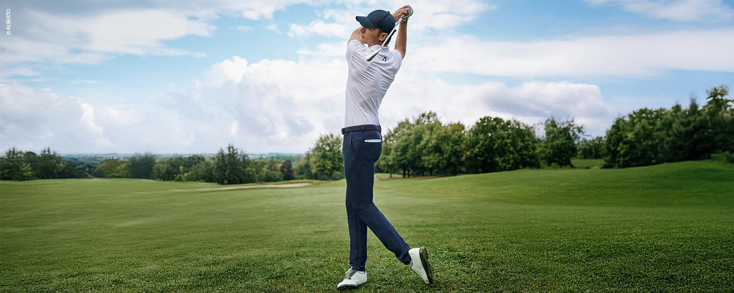 Dunkelblaue Golfhose in schmalem Schnitt, kombiniert mit weißem Poloshirt und Cap, getragen beim Abschlag auf dem Golfplatz.