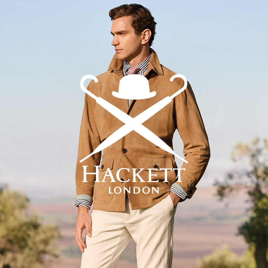 Mann in hellbraunem Sakko von Hackett mit Hemd und Krawatte, kombiniert mit weißer Hose, stehend im Freien mit Landschaft im Hintergrund