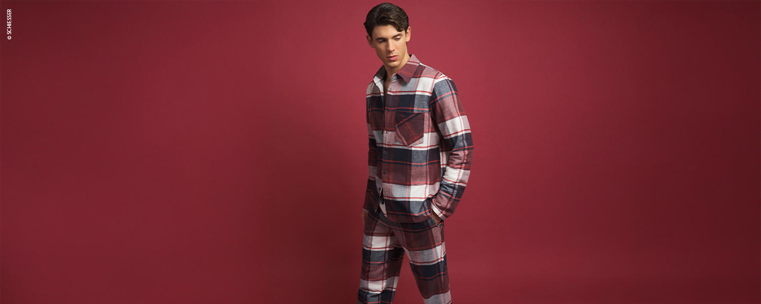 Ein Mann trägt einen karierten Pyjama mit langem Oberteil und langer Hose.
