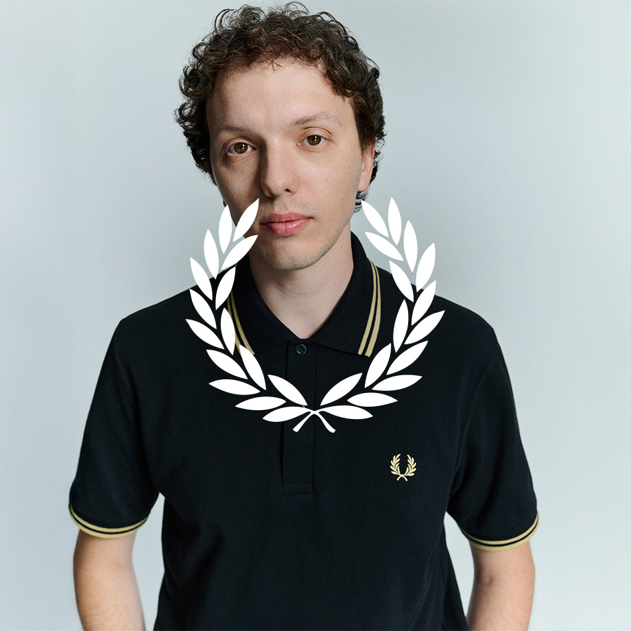 Mann in schwarzem Poloshirt von Fred Perry mit gelben Details am Kragen und Ärmelbündchen, vor neutralem Hintergrund.