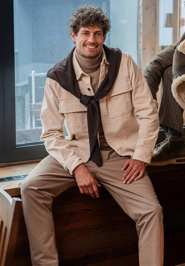Mann in beigefarbener Cordjacke mit Rollkragenpullover und braunem Pullover über die Schultern gelegt