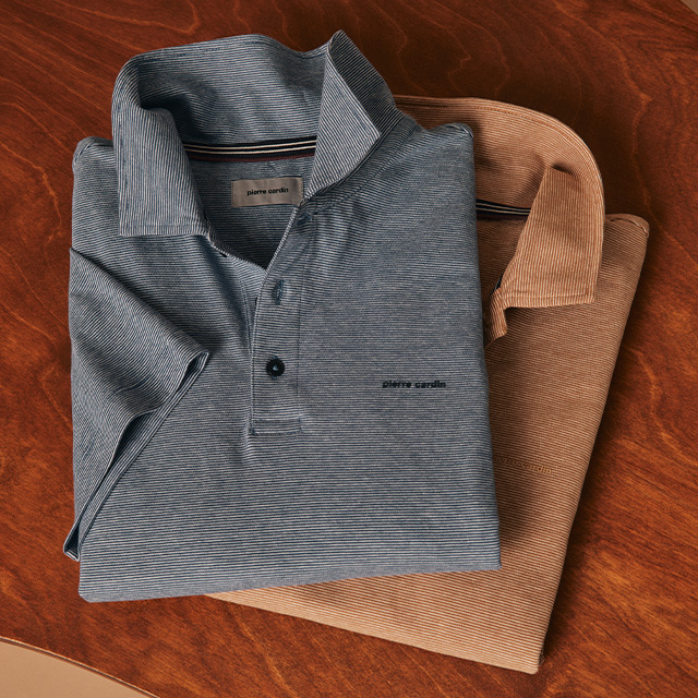 Zwei Poloshirts in Blau und Beige mit feinem Streifenmuster, gefaltet auf Holztisch