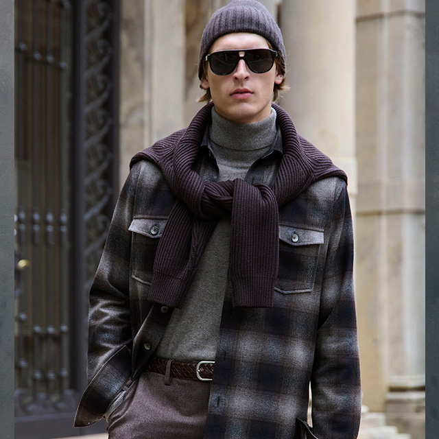 Mann in grauer Wolljacke mit Karomuster, grauem Rollkragenpullover und Strickpullover um die Schultern