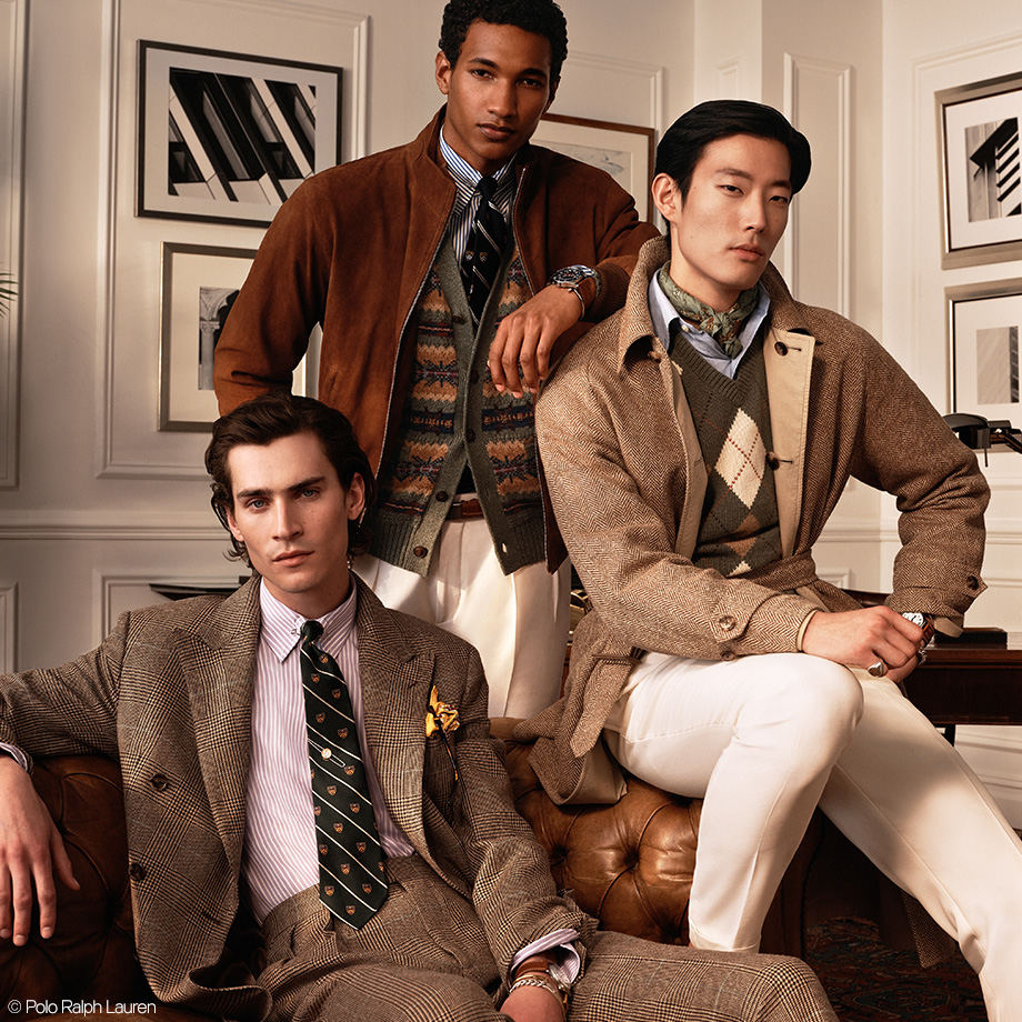 Drei Männer in klassisch-zeitlosen Outfits mit Tweed, Pullover und Sakkos in einer edlen Bibliothek. Verkörpert den typischen Preppy-Style von Polo Ralph Lauren.