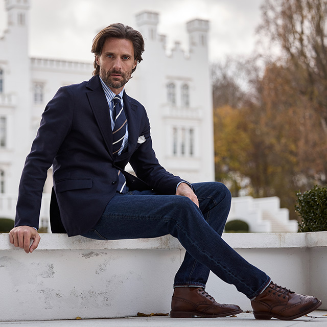 Navy Sakko mit Krawatte, kombiniert mit Jeans und braunen Lederboots, moderner Business-Casual Look.