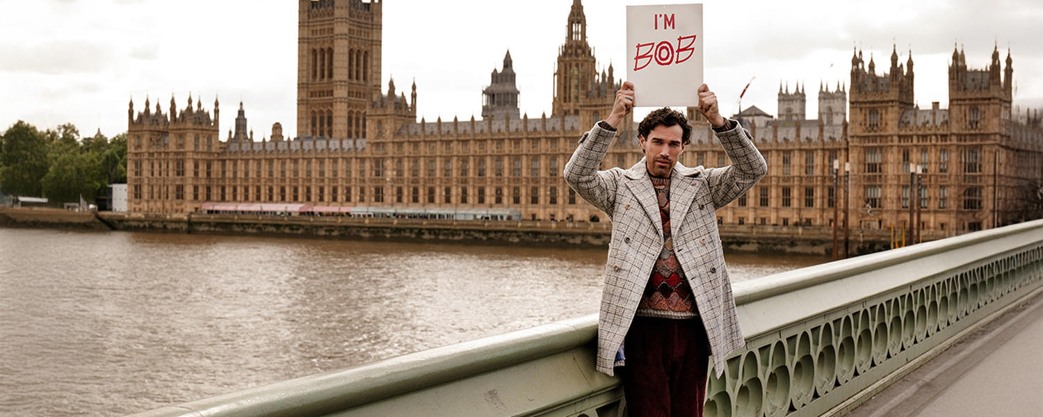 BOB markanter Look mit kariertem Mantel und Pullover im Muster-Mix, inszeniert vor den Houses of Parliament in London – stilvoll und individuell.