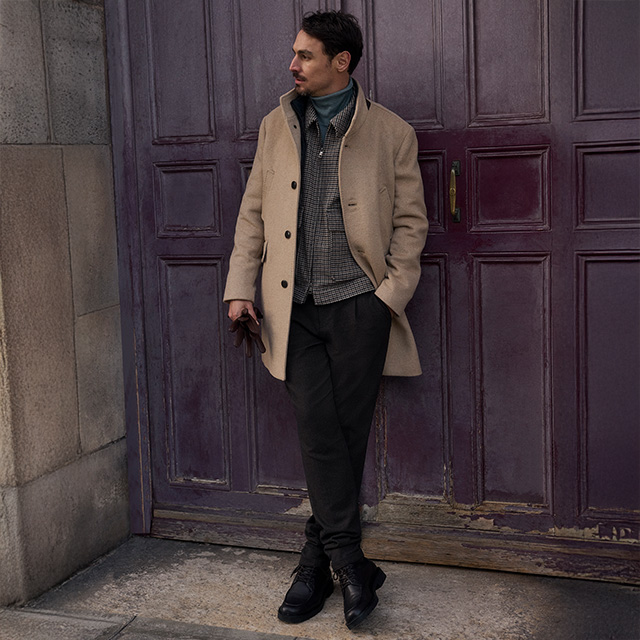 Beiger Mantel über Karo-Jacke und Rollkragen, kombiniert mit dunkler Hose und Sneakers, smarter Freizeit-Look.