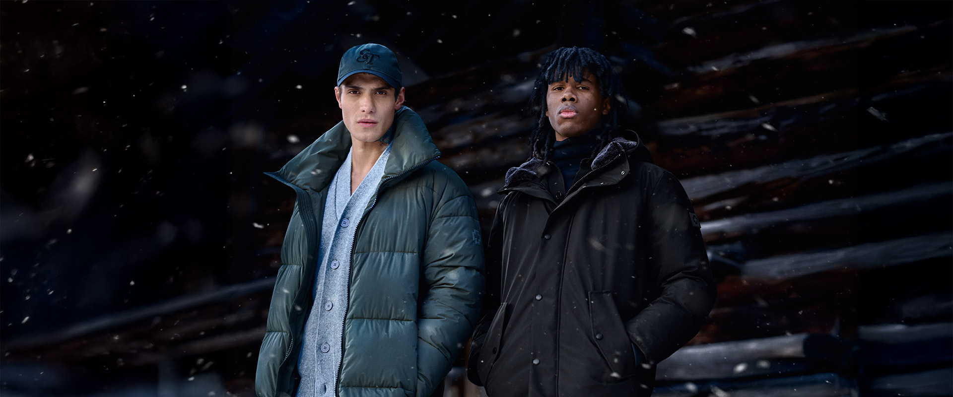 Winterlicher Streetstyle: grüne Daunenjacke mit Cap und schwarze Parka-Jacke im Schnee.