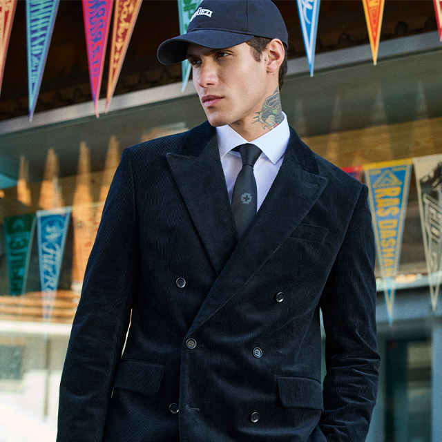 Schwarzer Cordanzug im Doppelreiher, kombiniert mit Hemd, Krawatte und Cap, urbaner Business-Look.