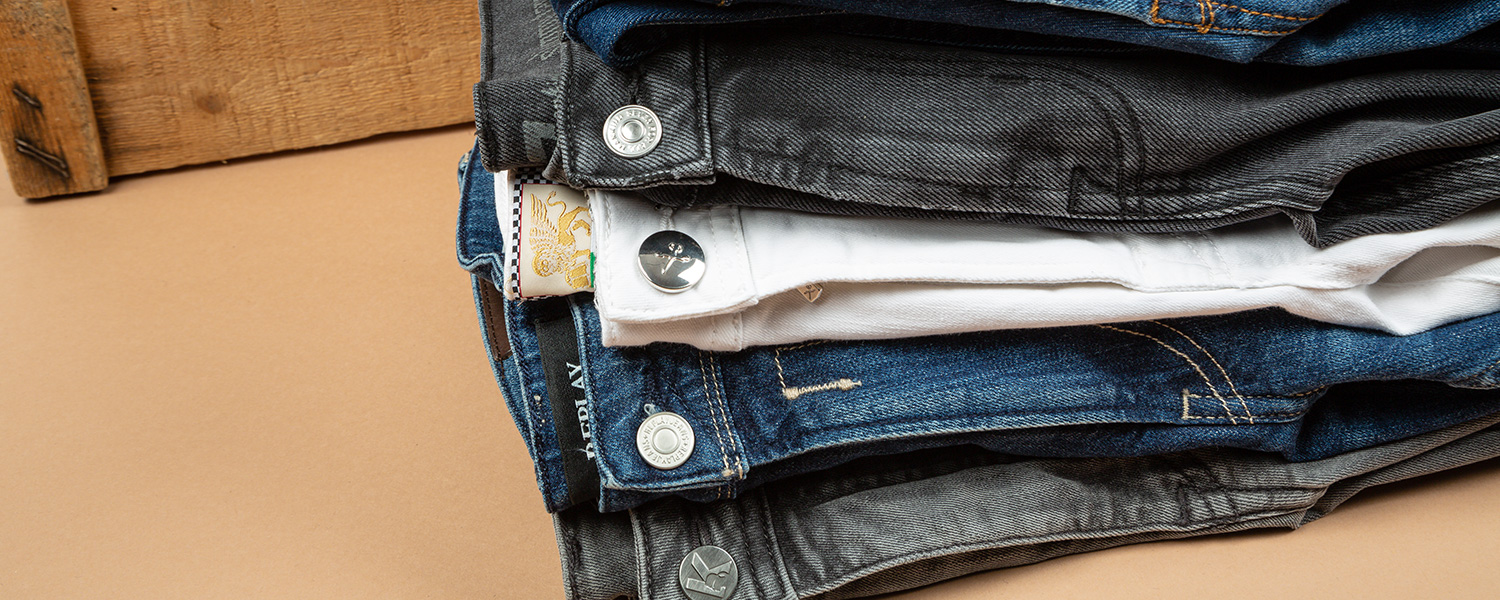 Stapel Jeans in verschiedenen Farben – von Schwarz über Weiß bis Blau, lässig kombiniert.