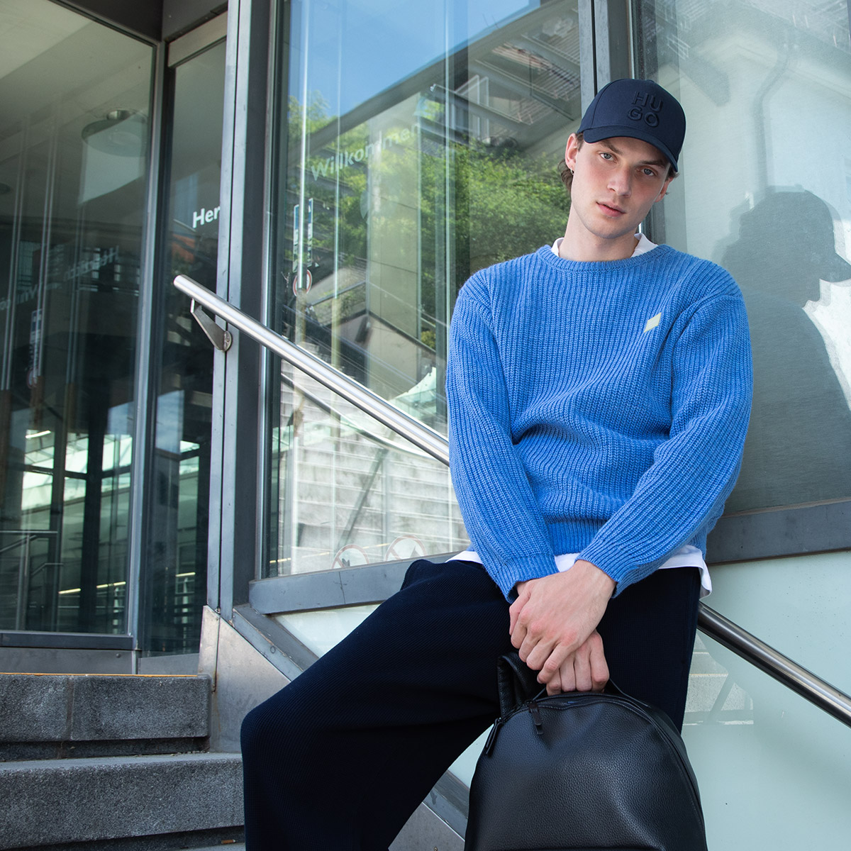 Blauer Strickpullover im lockeren Casual-Look, kombiniert mit Basecap und dunkler Hose.