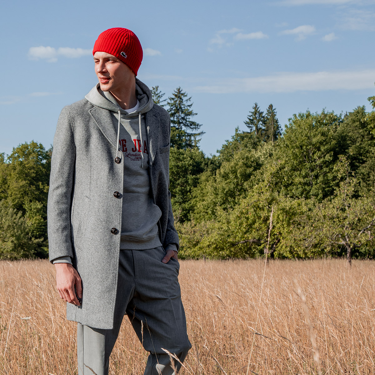 Grauer Wollmantel über Hoodie, kombiniert mit roter Beanie – urbaner Streetstyle im Alltag.