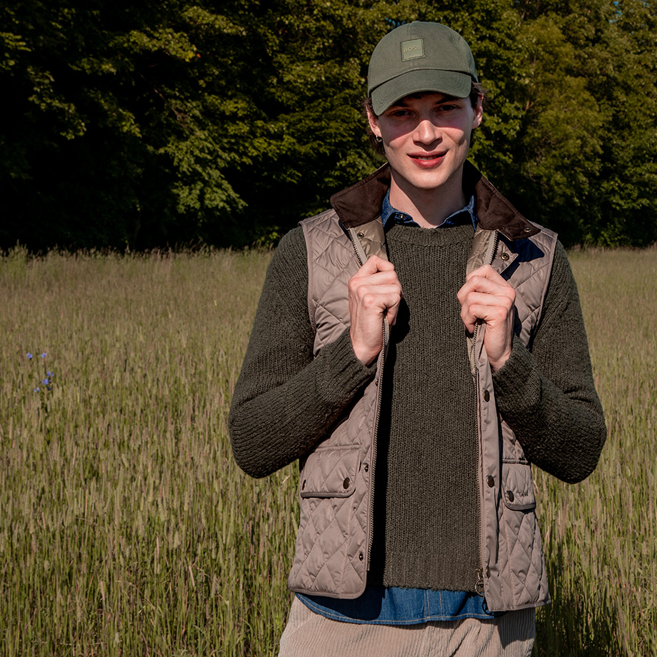 Steppweste in Beige über Strickpullover, kombiniert mit Cap – entspannter Outdoor-Style.