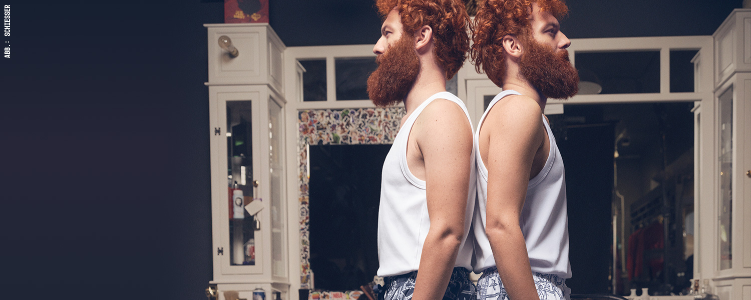 Zwei Männer mit Bart in weißen Tanktops, entspannter Retro-Look im Badezimmer.