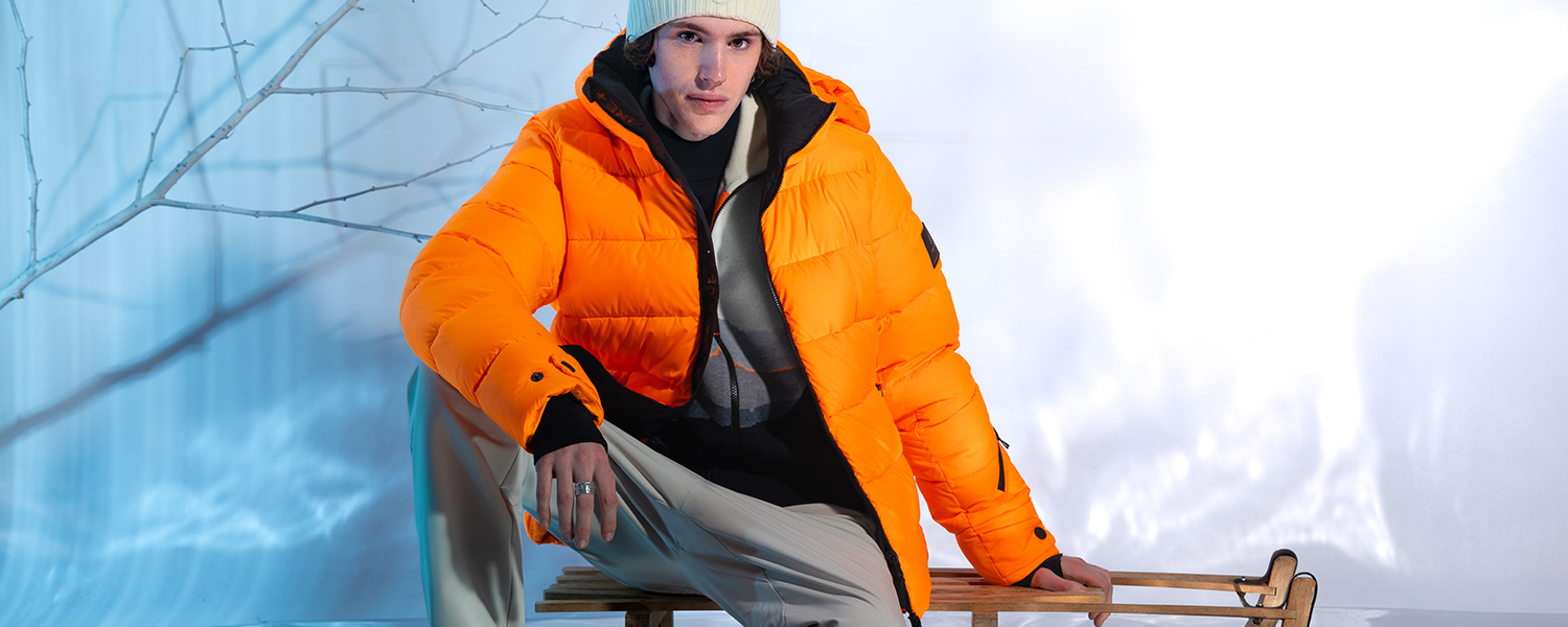 Orangefarbene Daunenjacke mit Beanie – sportlich-warmer Winterlook in leuchtenden Farben.