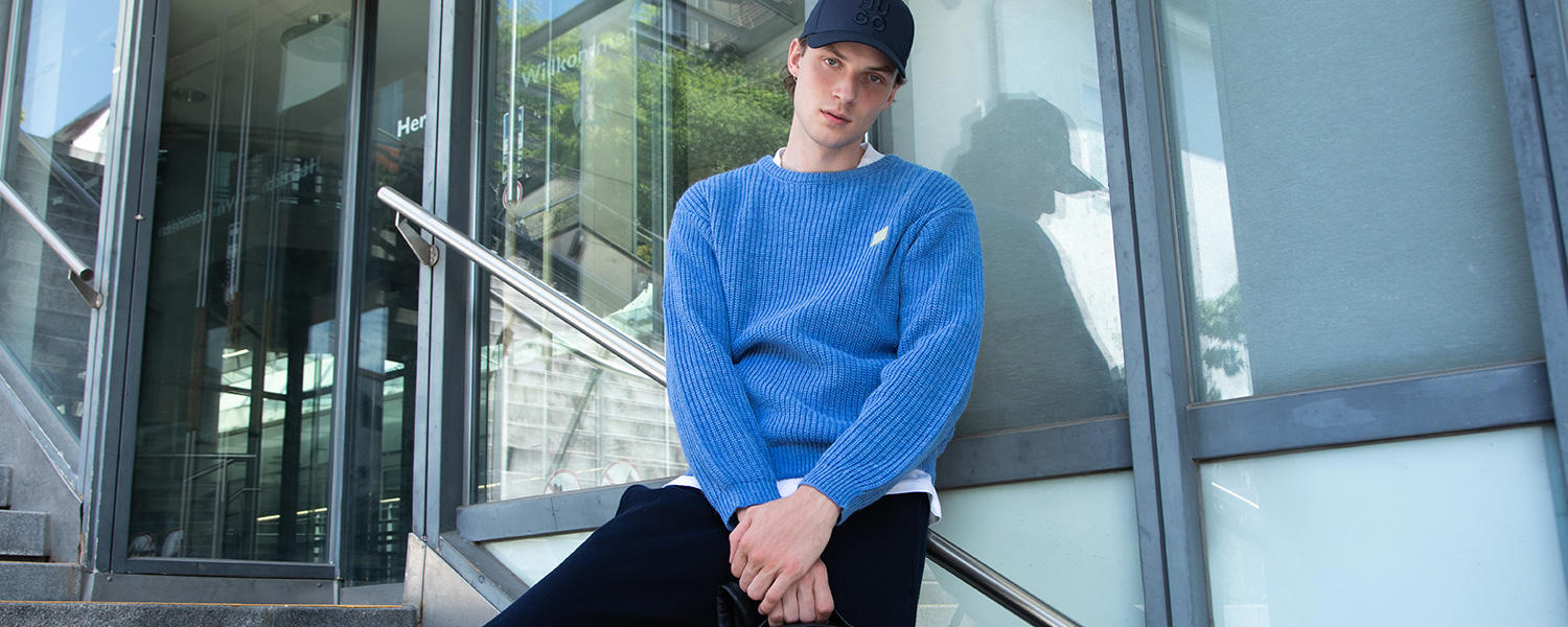 Blauer Strickpullover im lockeren Casual-Look, kombiniert mit Basecap und dunkler Hose.