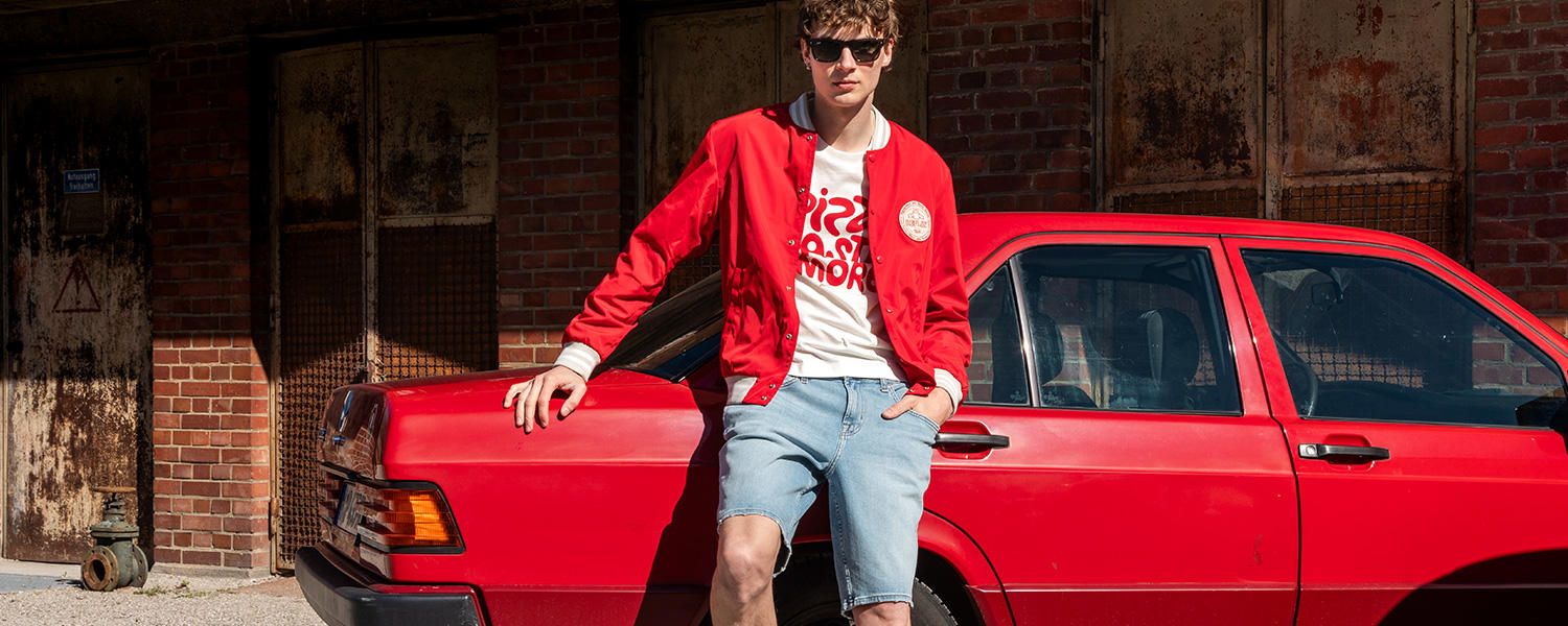 Jeansshorts mit roter Jacke – sommerlicher Retro-Look mit Statement-Shirt.