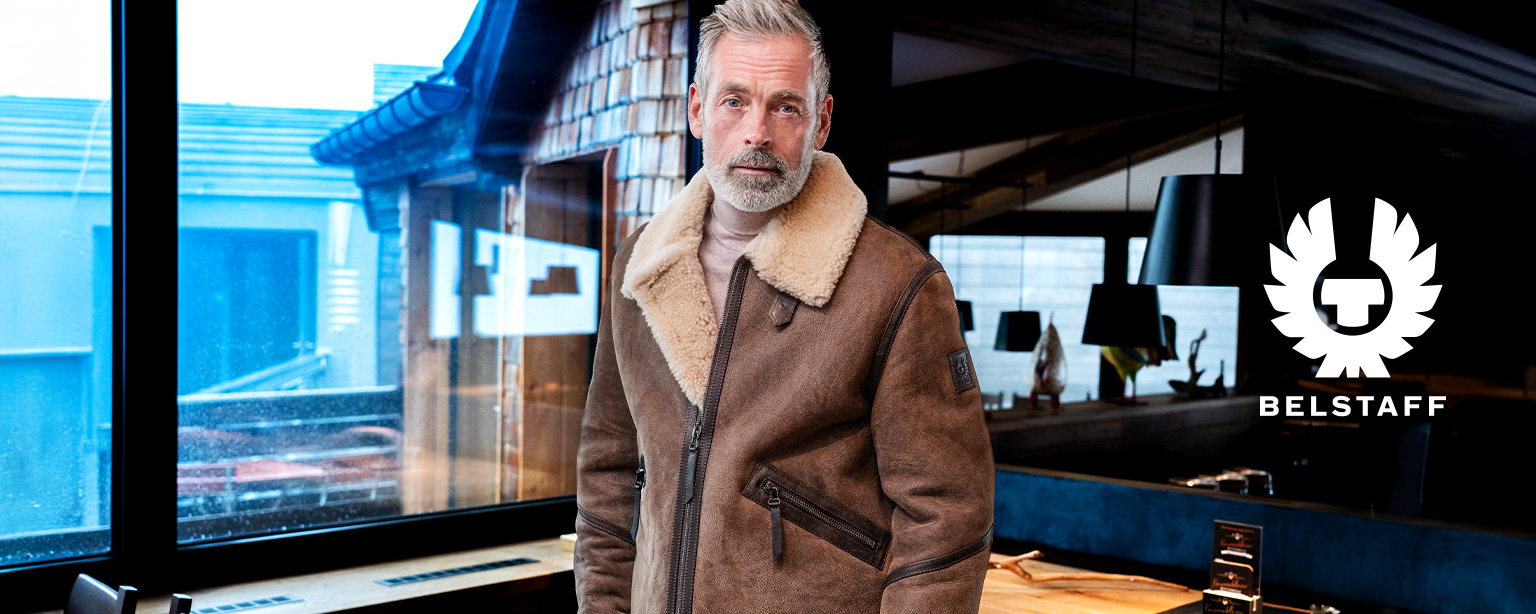 Mann trägt braune Leder-Fliegerjacke mit Lammfellbesatz von Belstaff in urbanem Setting.