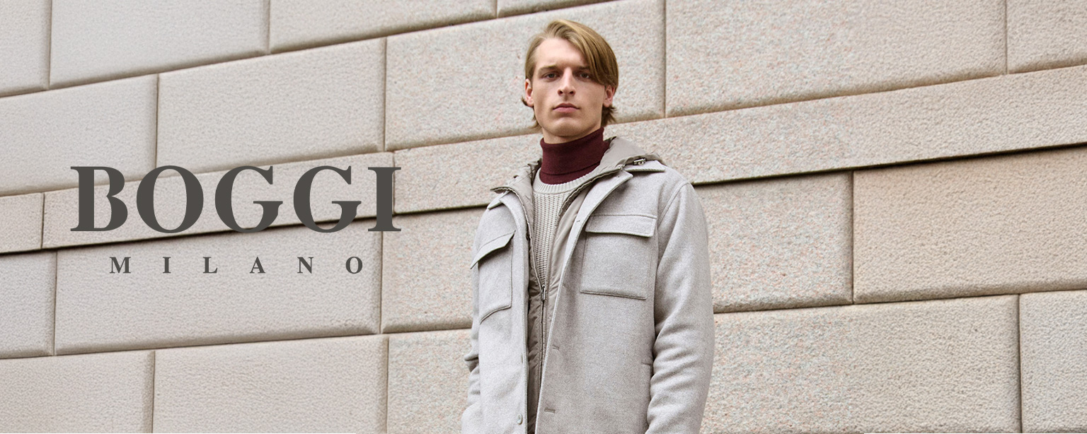 Mann trägt hellgraue Wolljacke über Rollkragenpullover und Hemd, posiert vor einer modernen Steinwand mit Logo von Boggi Milano.