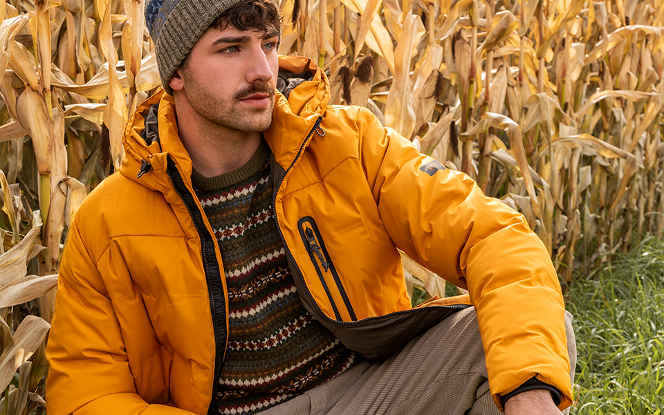Mann in gelber Steppjacke mit Strickpullover im Freien, Beige Mütze, lässiger Herbst-Look