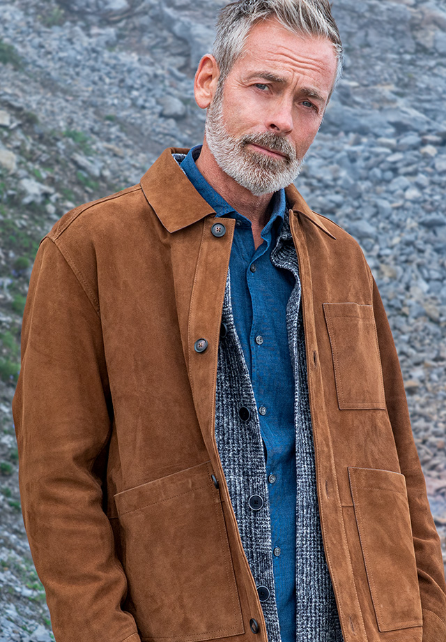 Hellbraune Wildlederjacke, blaues Hemd und grauer Pullover, lässig im Freien getragen