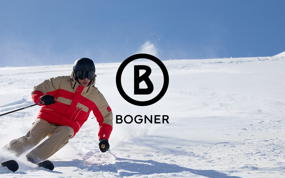 Skifahrer in beige-roter Skijacke mit Helm auf der Piste