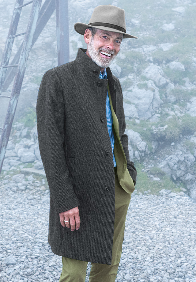 Herr in grauem Wollmantel und beigem Hut, elegant im Freien präsentiert
