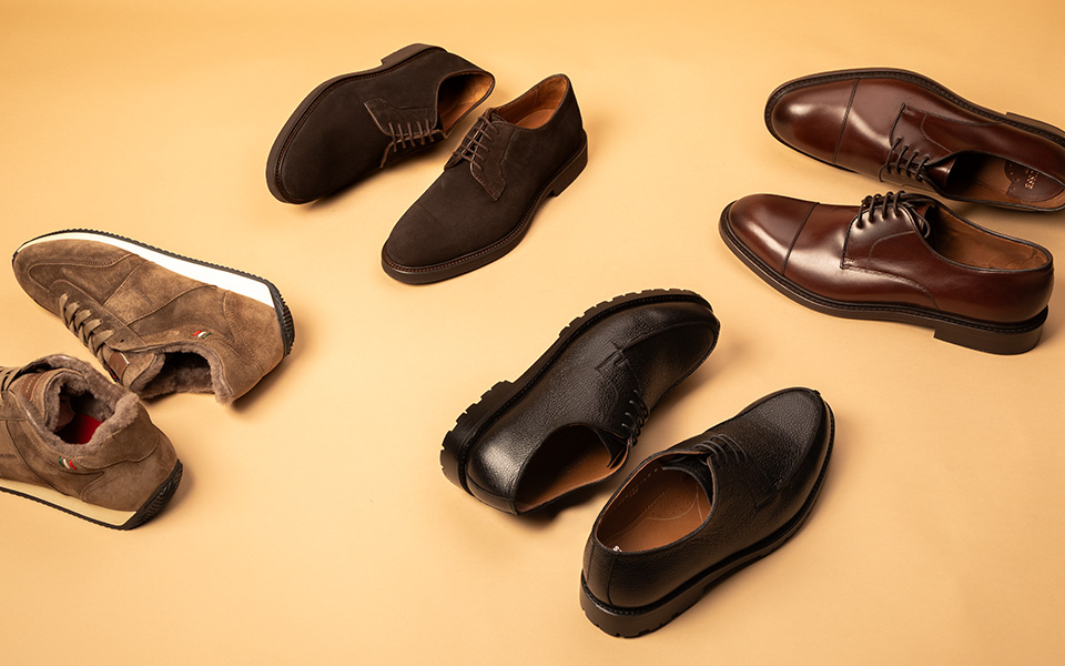 Elegante Herrenschuhe in Braun und Schwarz aus Leder und Wildleder, seitlich präsentiert auf beigem Hintergrund