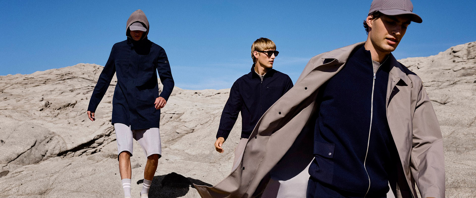 Drei Männer in navyblauen Jacken auf felsigem Terrain, legerer Freizeitlook
