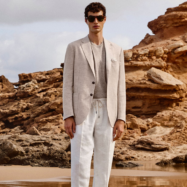 Herren-Sakko in Beige über grauem T-Shirt, kombiniert mit weißen Leinenhosen, in natürlicher Umgebung