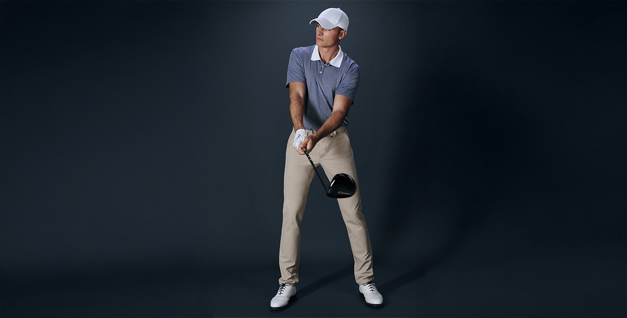 Herr in gemustertem, blauem Poloshirt und beiger Golfhose, Golfschläger haltend