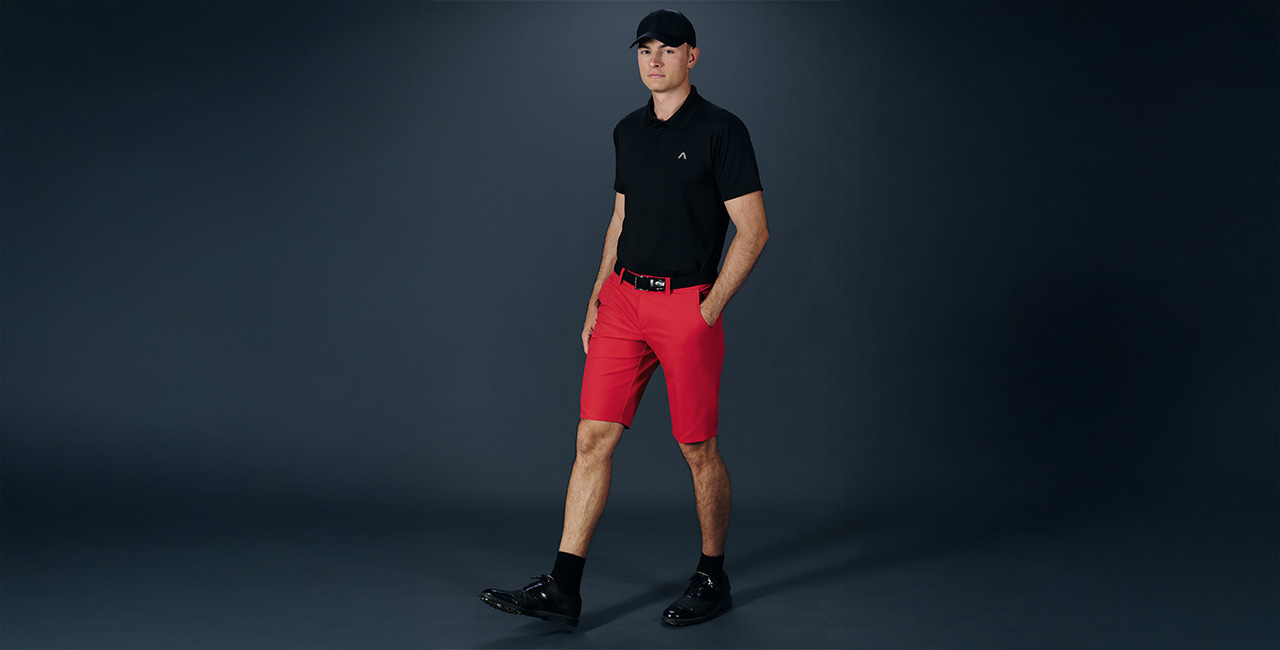 Herr in schwarzem Poloshirt und roten Shorts, sportlich elegant präsentiert