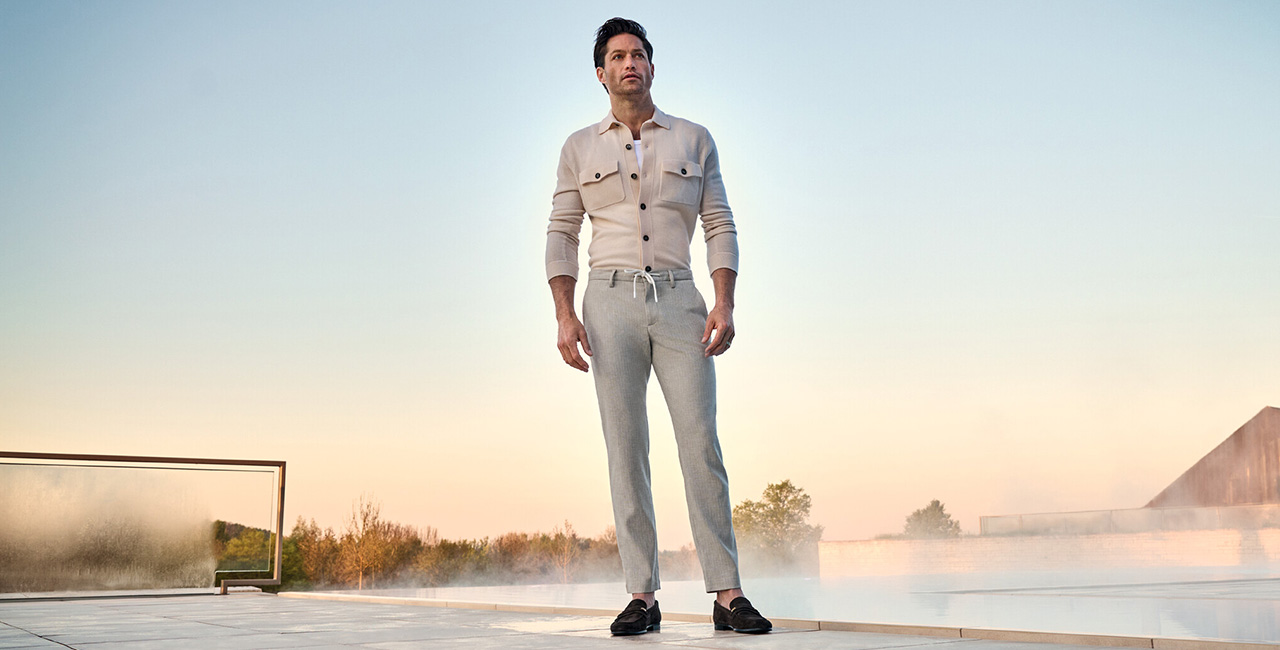 Mann in beiger Strickjacke mit Taschen und grauer Hose mit Tunnelzug, sportlich-elegant gestylt im Freien