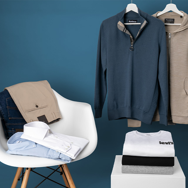 Ecru Strickpullover, grauer Kapuzenpullover, blauer Zip-Pullover auf Kleiderbügeln, gefaltete Jeans und Hemden auf Stuhl