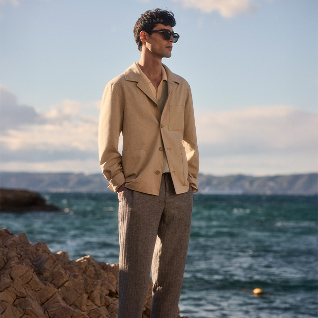 Mann in beiger Sommerjacke und grauer Hose am Meer, leger getragen