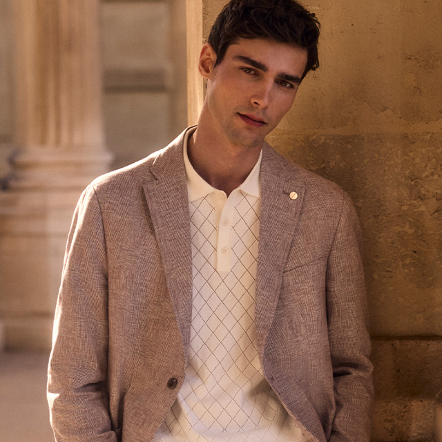 Beiger Herrenblazer aus Leinen, über weißem Poloshirt mit Rautenmuster, lässig getragen