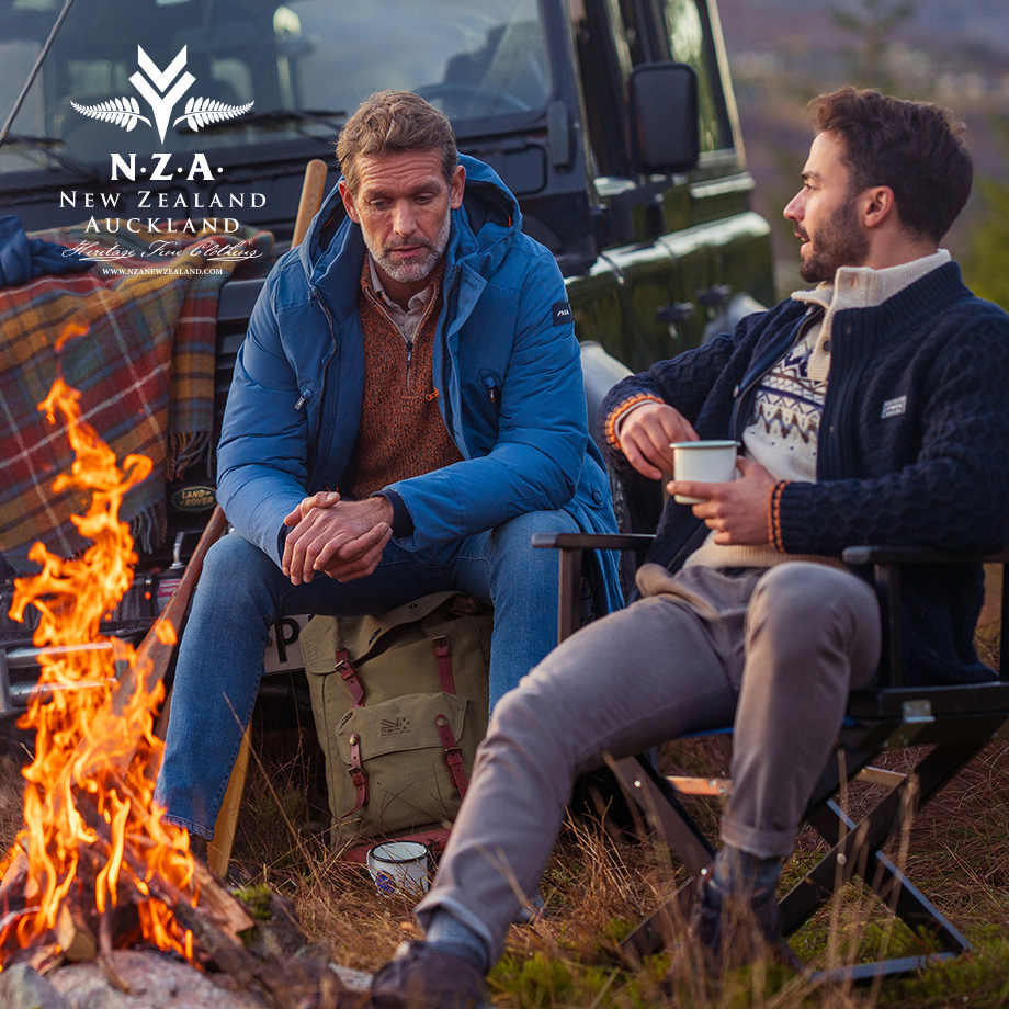 Männer in blauer Outdoor-Jacke und Strickpullover am Lagerfeuer, legerer Freizeit-Look